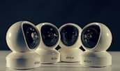 Four spherical security cameras with a glossy white finish are positioned in a row, each featuring a prominent lens and the brand name 'Briton' visible on their bases. The background is dark, contrasting with the brightly lit cameras.