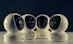 Four spherical security cameras with a glossy white finish are positioned in a row, each featuring a prominent lens and the brand name 'Briton' visible on their bases. The background is dark, contrasting with the brightly lit cameras.