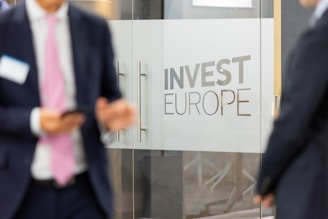 Personas de negocio hablando y con los moviles. Puertas de cristal y cartel de inversion en Europa