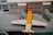 A detailed Lego model of an airport terminal with a plane parked at the gate. The building is made of white Lego bricks with blue windows, and the plane has a distinctive yellow and white color scheme. The scene includes jet bridges connecting the plane to the terminal.