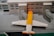 A detailed Lego model of an airport terminal with a plane parked at the gate. The building is made of white Lego bricks with blue windows, and the plane has a distinctive yellow and white color scheme. The scene includes jet bridges connecting the plane to the terminal.