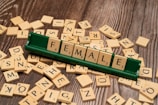 Wooden alphabet tiles are scattered on a wooden surface with a green tile holder displaying the word 'FEMALE' using the tiles.