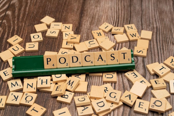 Wooden letter tiles scattered across a wooden surface, with a green tile holder displaying the word 'PODCAST' spelled out prominently.