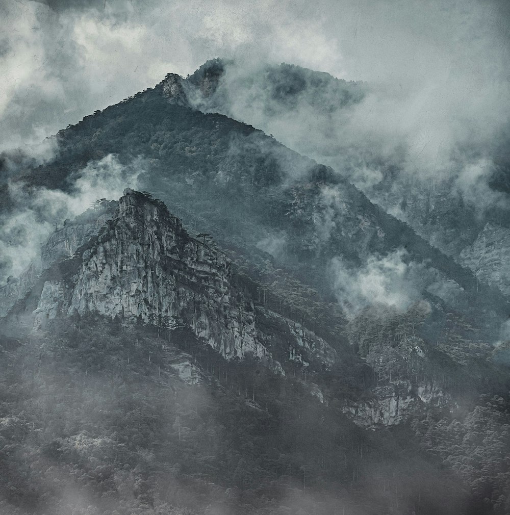 a black and white photo of a mountain covered in clouds