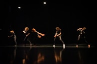 Silhouettes of dancers moving expressively against a dark background with subtle colored lights.