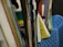 A collection of textbooks and notebooks in various colors with visible spines. Some of the books include subjects like English and sciences. The materials are organized upright in a blue plastic basket.