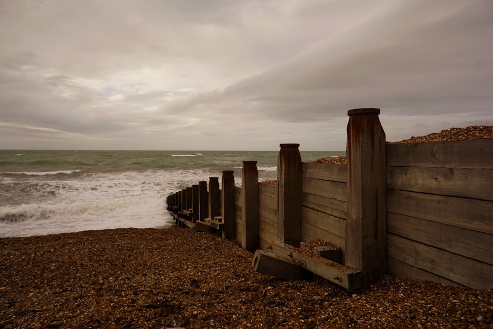 a wooden fence next to the ocean on a cloudy day