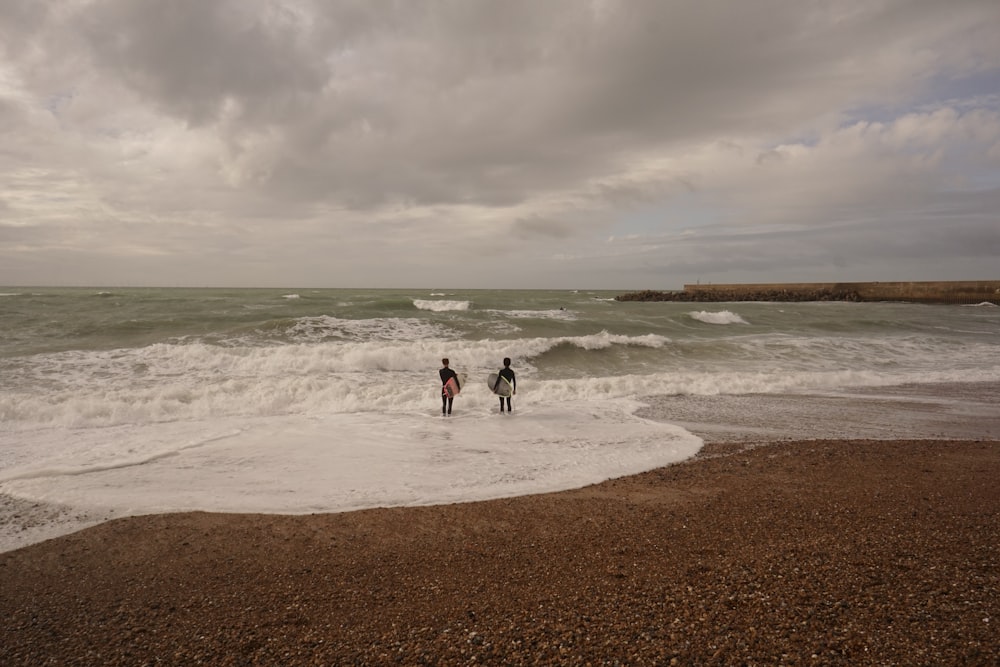 two people standing in the surf on a cloudy day