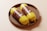 Two yellow packaged sausage mock-ups placed in a round woven basket on a light surface. The packaging features brown labels with text and the letters 'MF'.