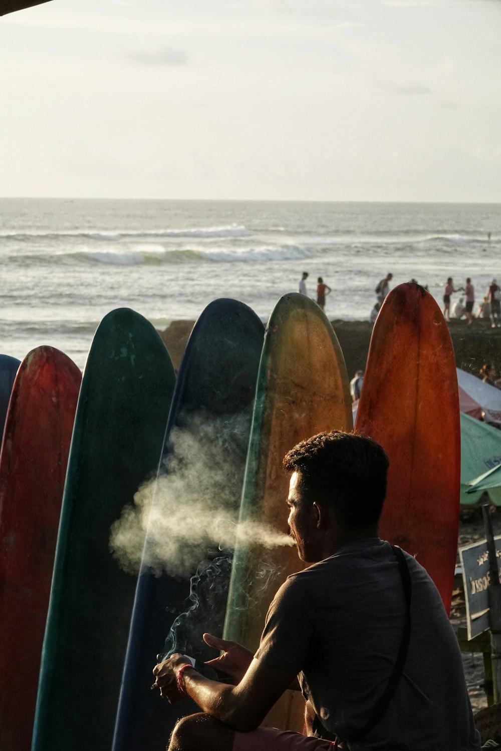 Un hombre sentado en un banco junto a una fila de tablas de surf