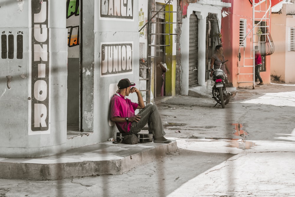 a man sitting on the side of a building talking on a cell phone