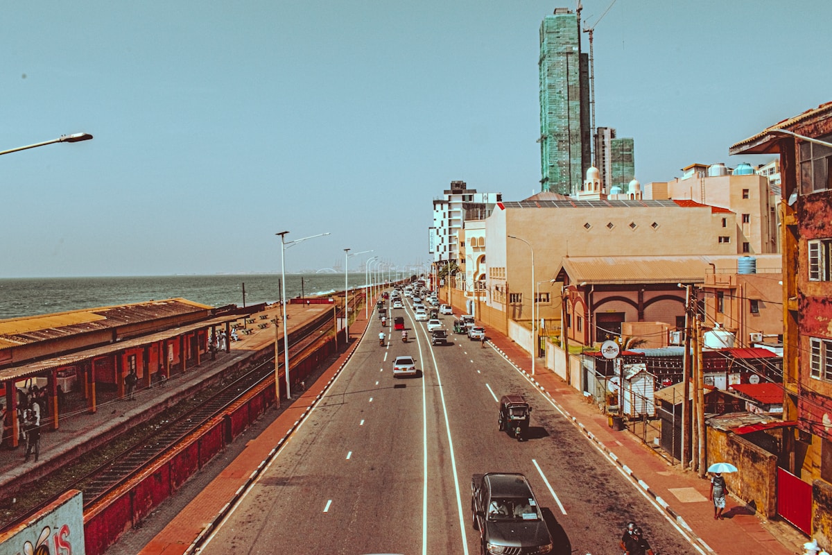 Colombo's main coastal highway with modern buildings, the Lotus Tower, and the Indian Ocean in the background - a city in active transformation with new transit infrastructure
