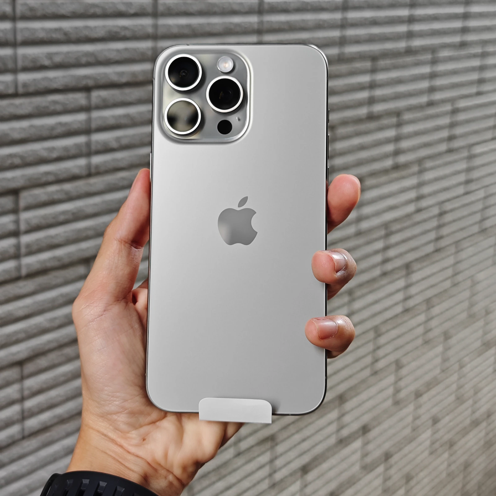 Modern iPhone Pro Max in white titanium held in hand, triple-lens camera and Apple logo visible