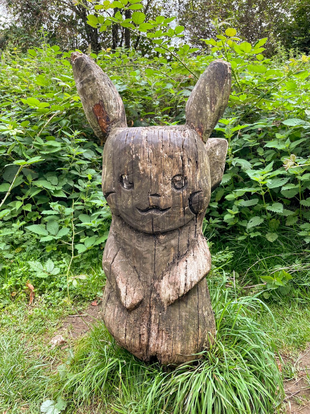 a wooden statue of a rabbit sitting in the grass