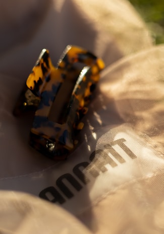 Close-up of a sleek, flexible hair clip resting on soft khaki green fabric.