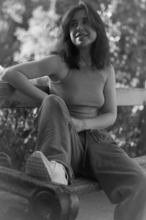 A relaxed pose of a woman in a flowing, earth-toned outfit sitting on a wooden bench.
