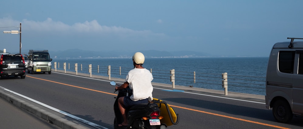 A happy rider cruising along a sunny coastal road on a sleek scooter from Zing Rentals.