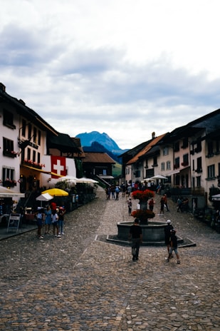 An old cobblestone street in a Swiss village, lined with colorful flowers and historic buildings under a clear blue sky.
