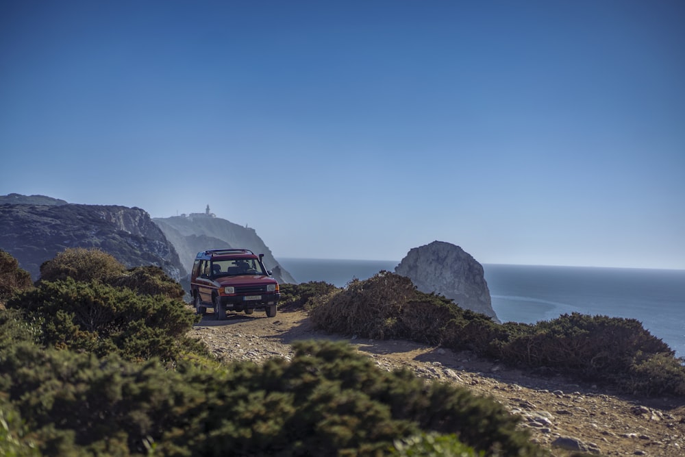 a jeep driving down a dirt road next to the ocean