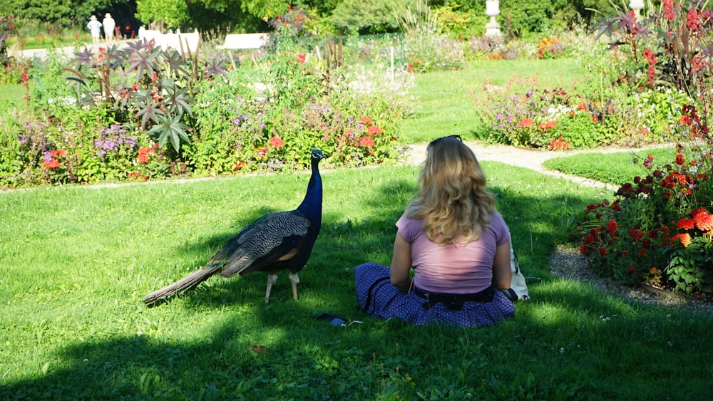 a woman sitting on the ground next to a peacock
