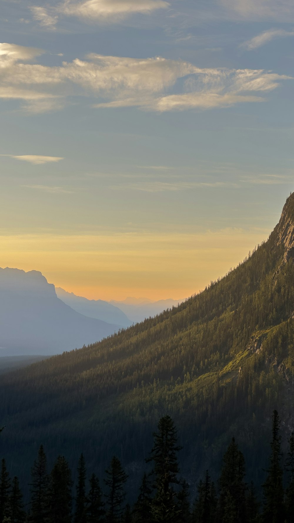 the sun is setting on a mountain with trees