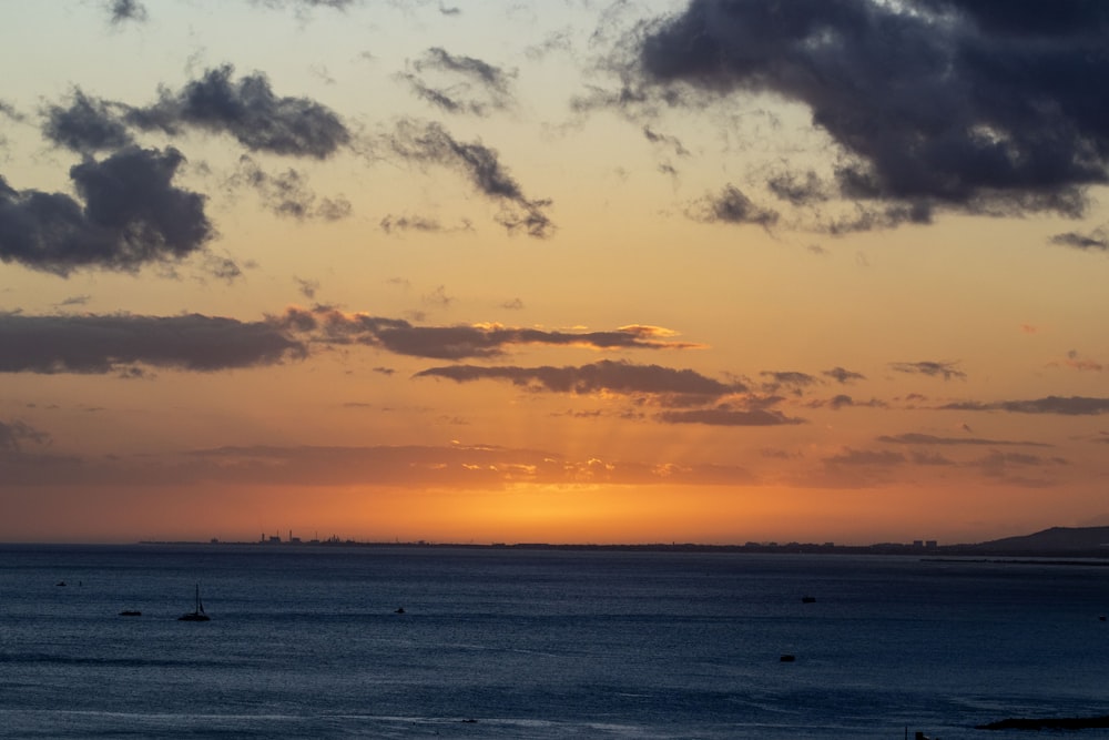 the sun is setting over the ocean on a cloudy day