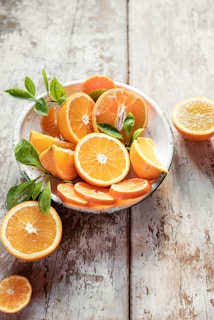Close-up of vibrant orange peel powder in a rustic wooden bowl surrounded by fresh oranges and green leaves.