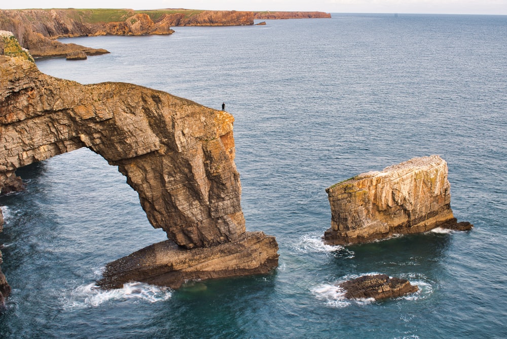 a person standing on top of a rock formation in the ocean