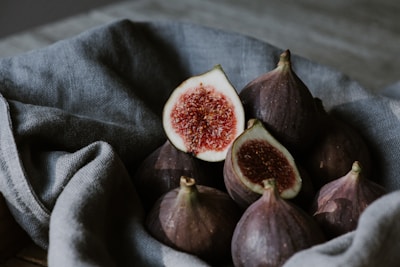 A collection of fresh figs resting on a textured cloth, with one fig sliced open to reveal its rich, red interior. The figs have a deep purple hue, and the lighting provides a rustic and natural ambiance.