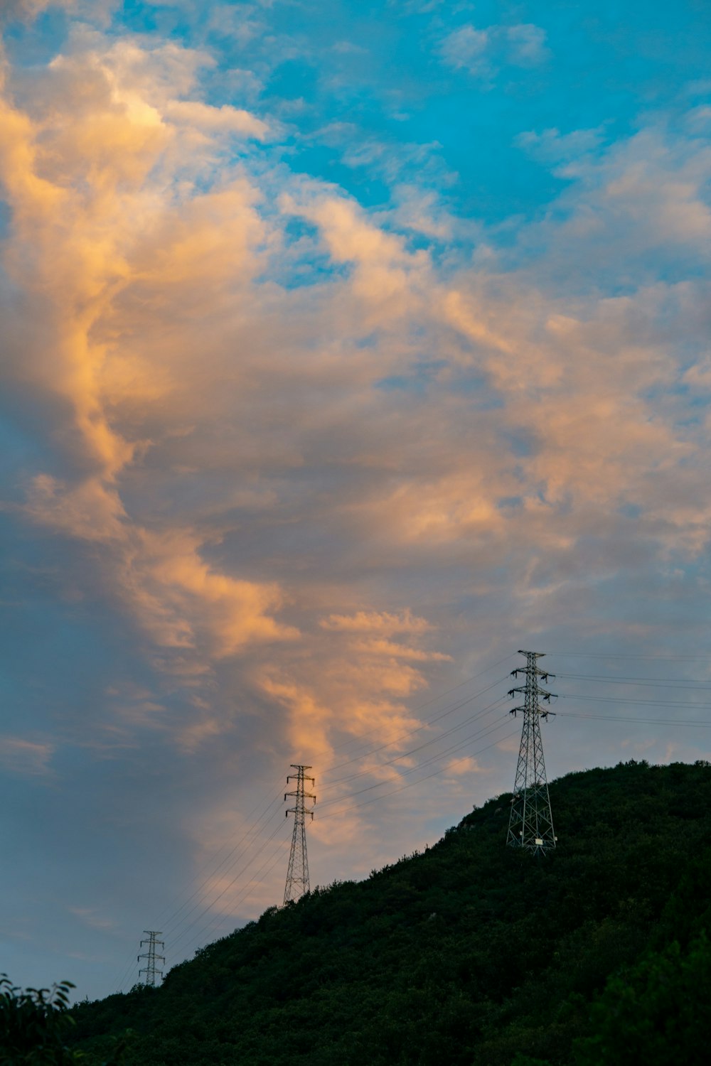 une colline surmontée de lignes électriques sous un ciel nuageux
