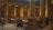 A grand library interior with large columns and high ceilings, where numerous people are reading and studying at wooden tables. Shelves filled with books line the walls, and there is a spiral staircase in the background. The atmosphere is quiet and focused.
