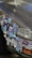 A car's front bumper and side panel are covered with an array of colorful stickers. These include various designs such as cartoon characters, logos, symbols, and abstract art. The car appears to be parked on a paved surface, and the paint shows signs of wear.