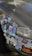 A car's front bumper and side panel are covered with an array of colorful stickers. These include various designs such as cartoon characters, logos, symbols, and abstract art. The car appears to be parked on a paved surface, and the paint shows signs of wear.