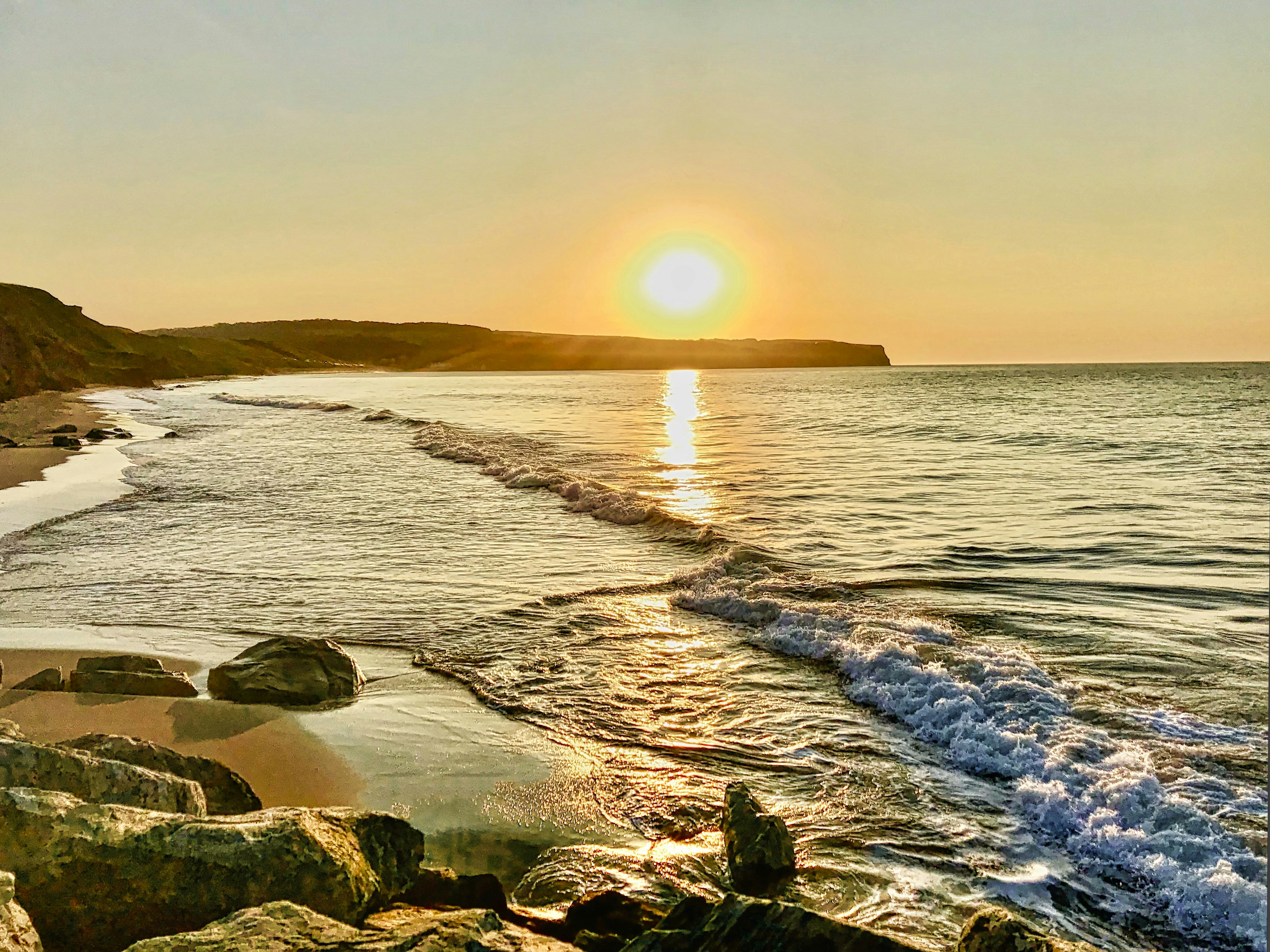the sun is setting over the water at the beach