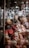 A collection of dolls is on display, some wrapped in plastic. The dolls have various hair colors and styles, and they are positioned on a street vendor's stall. In the background, there are multiple blurred objects and lights.