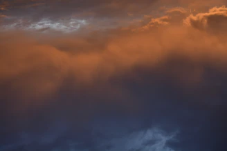 a plane flying through a cloudy sky at sunset
