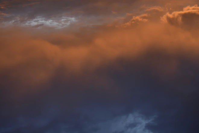 a plane flying through a cloudy sky at sunset