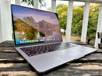 A peaceful outdoor scene featuring a laptop on a wooden table surrounded by nature.