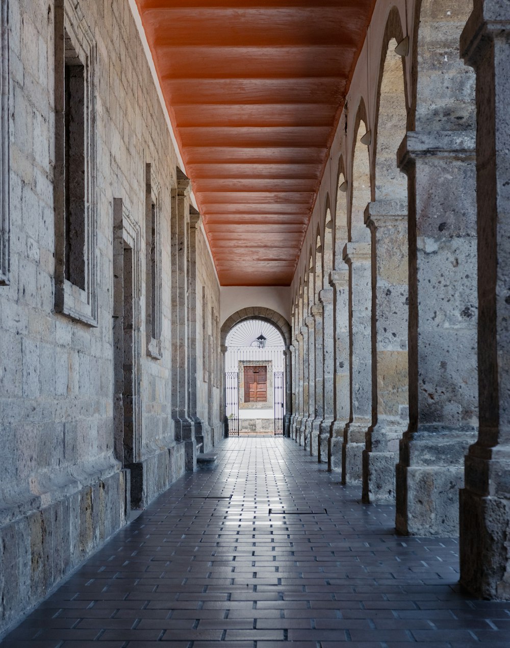 a long hallway with stone pillars and a red ceiling