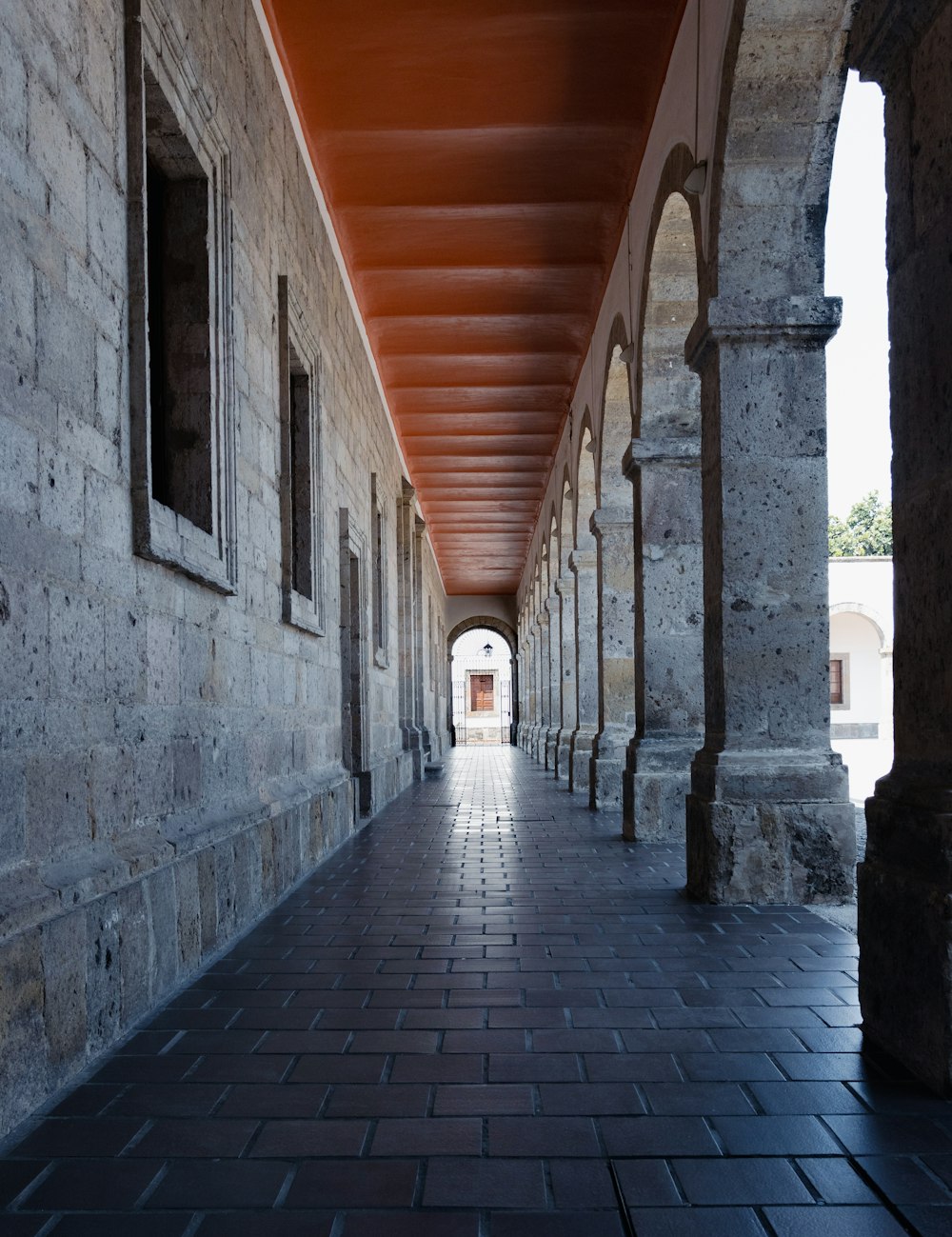 a long hallway with stone pillars and a red roof