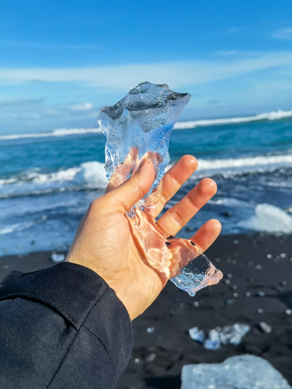 a hand holding a piece of ice on a beach