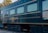 A vintage train car with the name 'Jose Cuervo Express' displayed prominently in decorative gold lettering. The train is dark blue with horizontal lines running along the body, and the windows have a light tint. The setting is outdoors with visible greenery and utility poles in the background.
