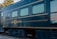 A vintage train car with the name 'Jose Cuervo Express' displayed prominently in decorative gold lettering. The train is dark blue with horizontal lines running along the body, and the windows have a light tint. The setting is outdoors with visible greenery and utility poles in the background.