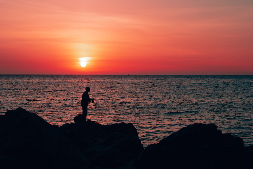 eine Person, die bei Sonnenuntergang auf einem Felsen in der Nähe des Ozeans steht