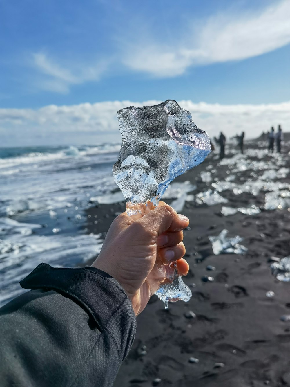 a hand holding a piece of ice on a beach