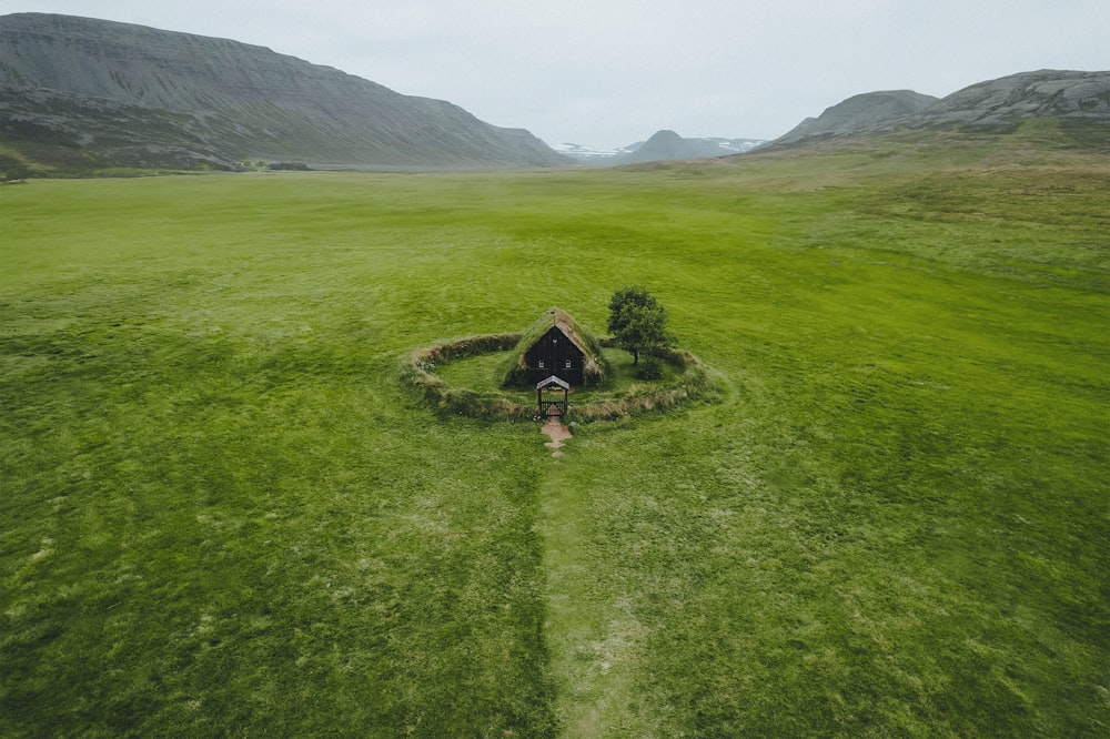 an aerial view of a grassy field with a small hut in the middle