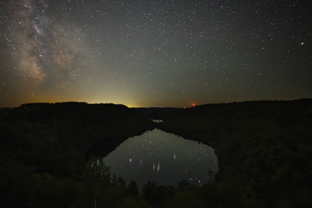 a lake surrounded by trees under a night sky