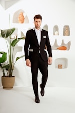 Man wearing a sleek black formal suit in a minimalist white and gold styled room.