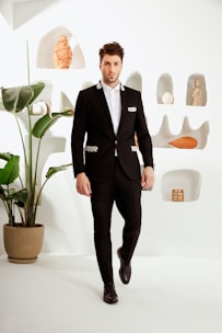 Man wearing a sleek black formal suit in a minimalist white and gold styled room.
