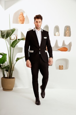 A stylish man in a sleek black suit against a minimalist backdrop.